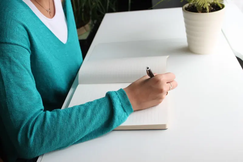 Person schreibt in ein Notizbuch am Schreibtisch